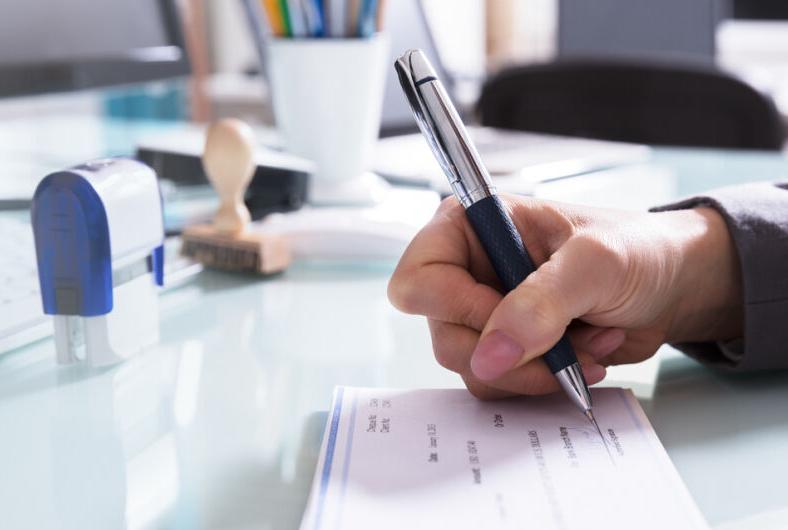 Businessman Filling The Cheque On Desk